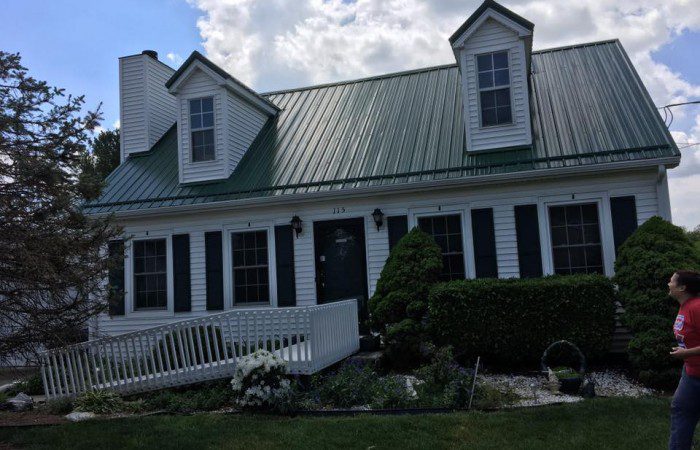 a woman is standing outside of a house with a green roof